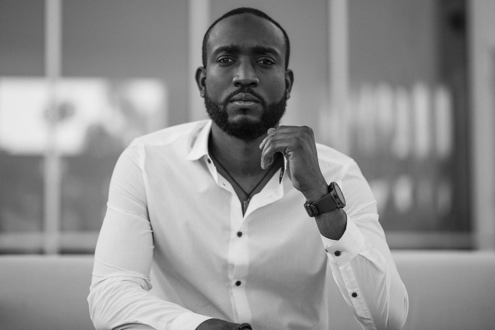 Black-and-white photo of a bearded man in a white shirt resting his chin on his hand