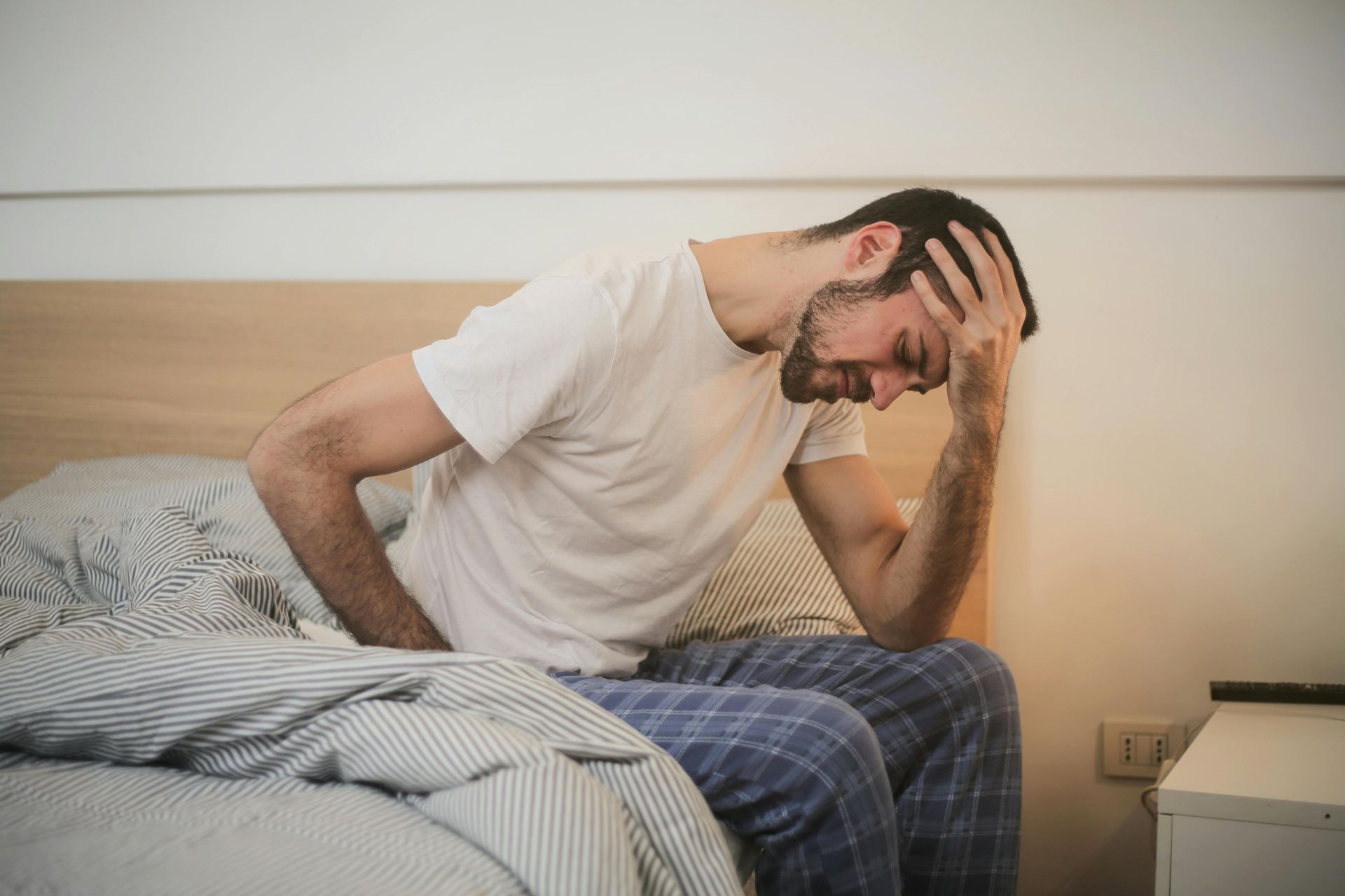 A man sits on the edge of a bed with his head in his hand