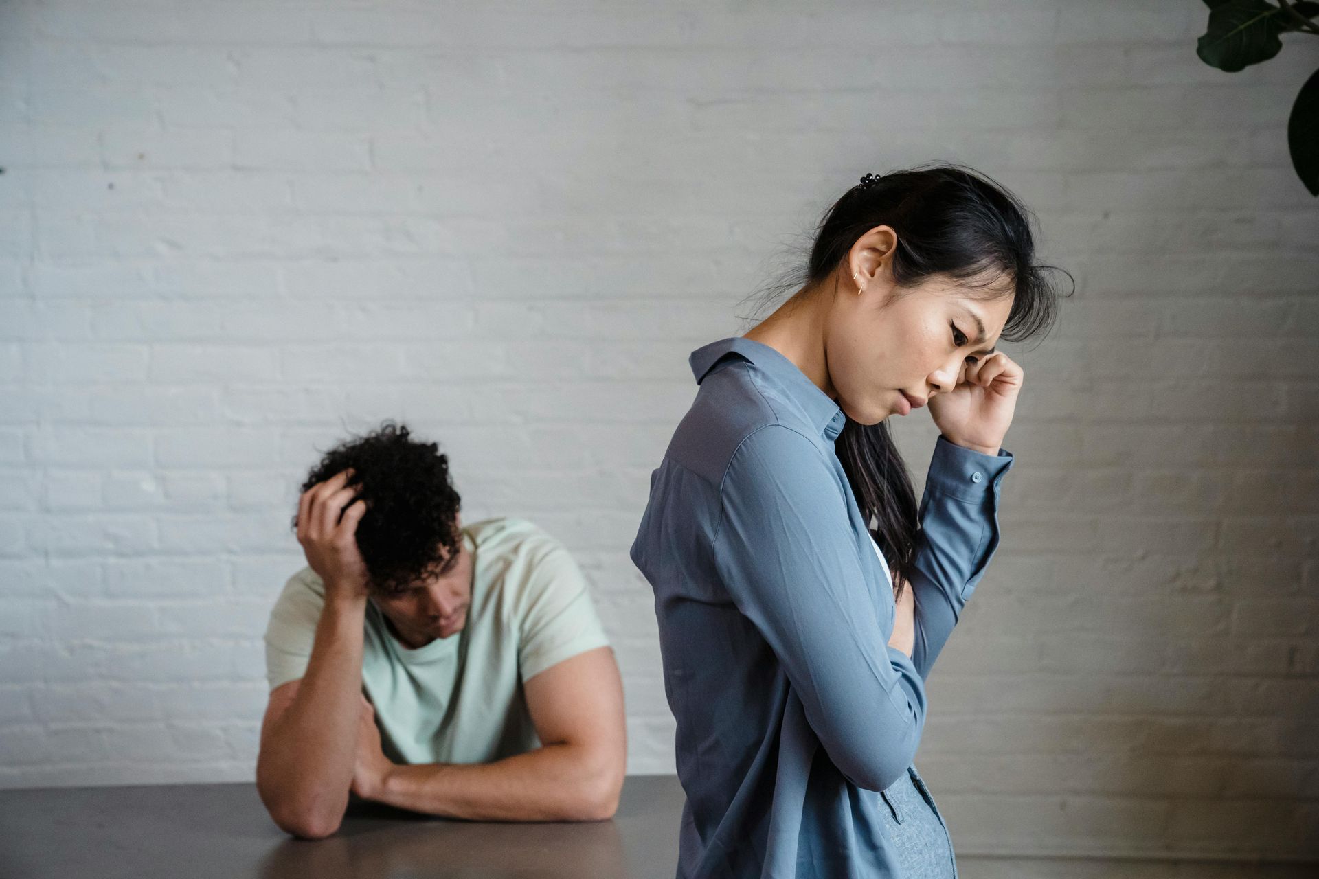 A couple stand back to back against a brick wall, showing tension and disconnection
